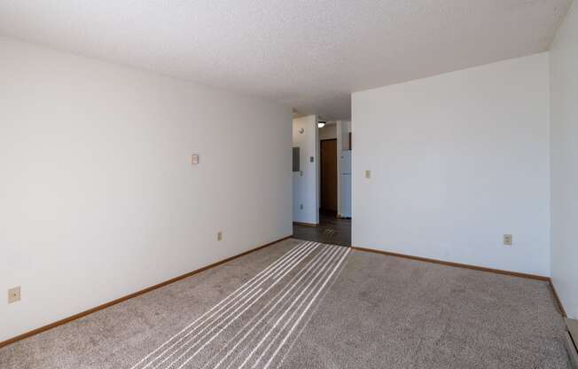 an empty living room with carpet and white walls. Grand Forks, ND Chandler 1866 Apartments