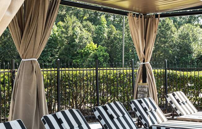 an outdoor lounge area with black and white striped lounge chairs and beige curtains
