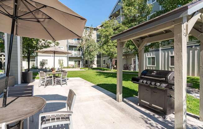 A patio with a grill and chairs under an umbrella.