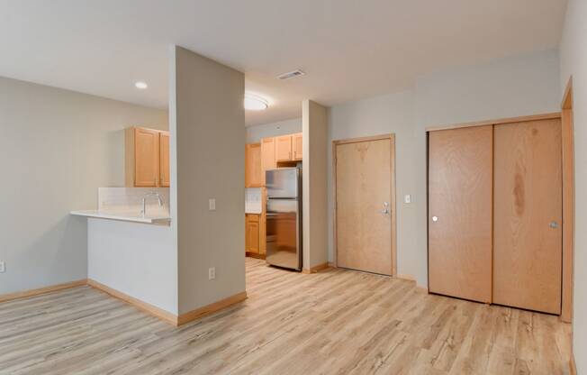 the living room and kitchen of an empty apartment with wood flooring and wooden cabinets