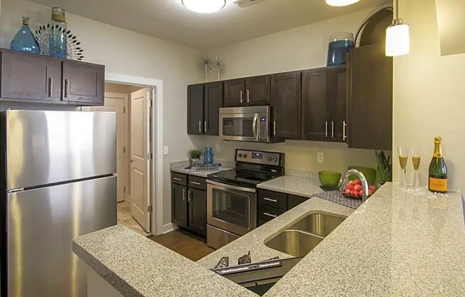 A kitchen with a refrigerator, microwave, oven, and sink.