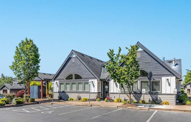 A parking lot in front of the leasing office and clubhouse with a tree in front of it at The Landing Apartments and Townhomes, Oregon, 97045