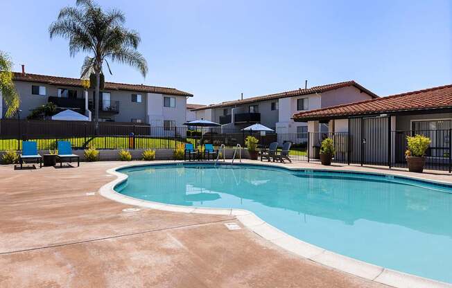 A pool surrounded by a black fence and palm trees.