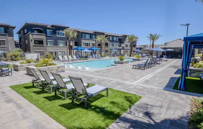 Sunny resort style pool area with sunbathing chairs, large pool, cabanas, all surrounded by apartment buildings.