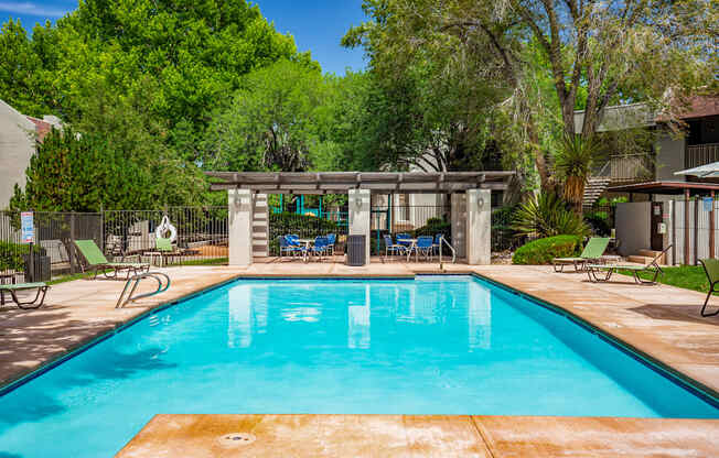A swimming pool surrounded by trees and chairs.