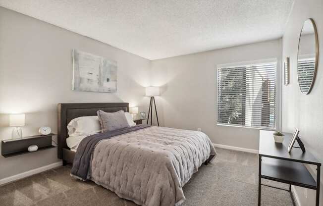 A bedroom with a bed, nightstand, and a window with blinds.