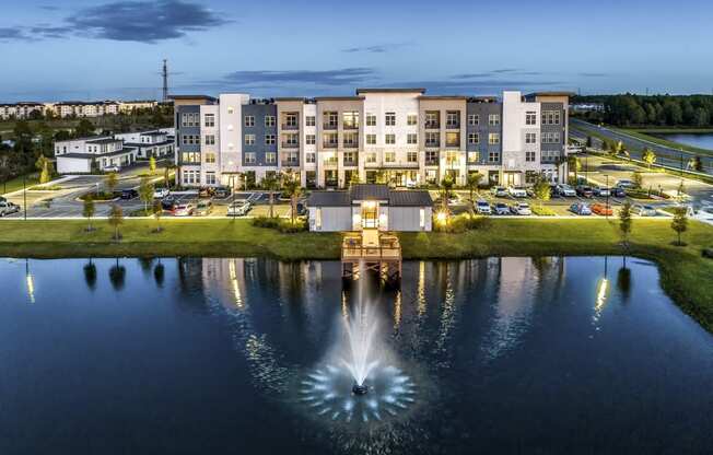 a fountain in the middle of a pond with an apartment building in the background at The Overlook, Winter Garden, 34787