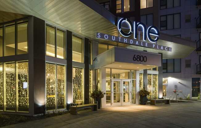 Outside shot of apartment building entrance with large illuminated sign reading "One Southdale Place" and the number "6800" above the front doors