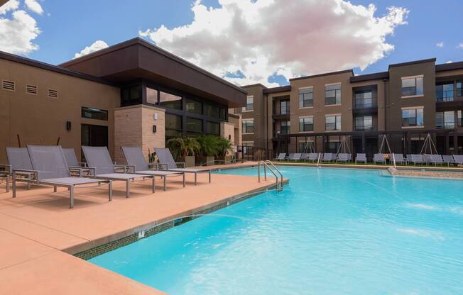 A swimming pool in front of a building with lounge chairs around it.