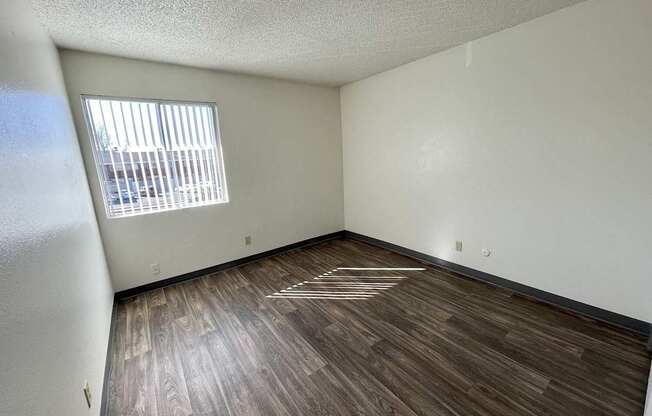 A room with wooden flooring and a window with blinds.