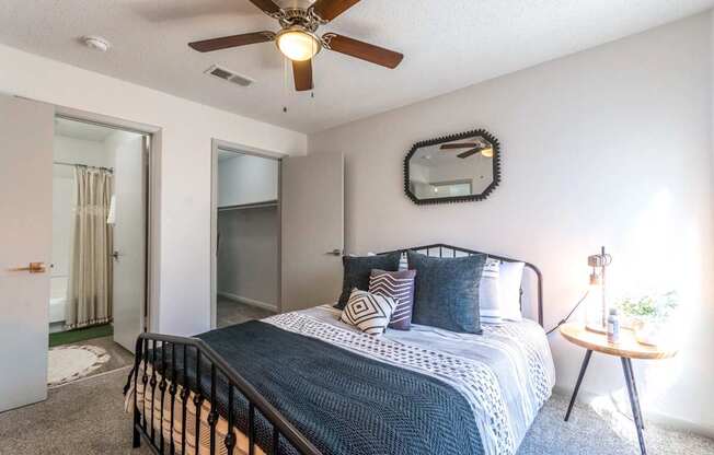 A bedroom with a bed, a ceiling fan, and a mirror on the wall.