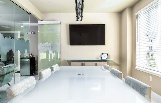 A conference room with a glass table and a television mounted on the wall.
