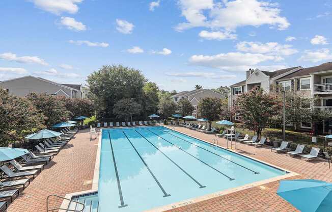 A large outdoor swimming pool surrounded by sun loungers and umbrellas.