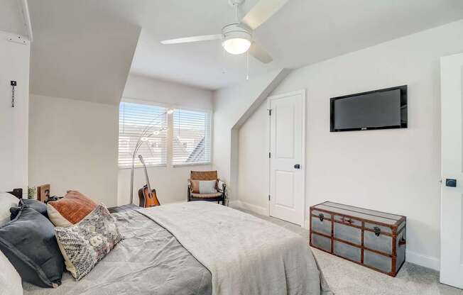 A bedroom with a bed, a chair, a guitar, and a ceiling fan.