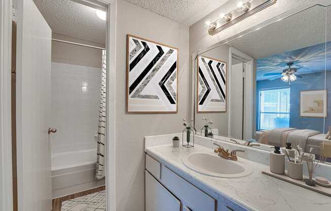 A bathroom with a white sink and a mirror with a light above it.