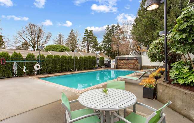 A table with a plant on it sits in front of a pool.