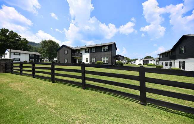 a black fence in front of a green field with houses in the background