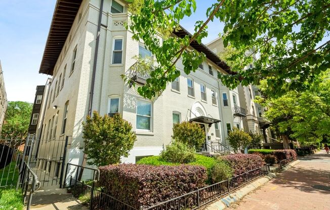 an apartment building with a sidewalk in front of it and trees in the background