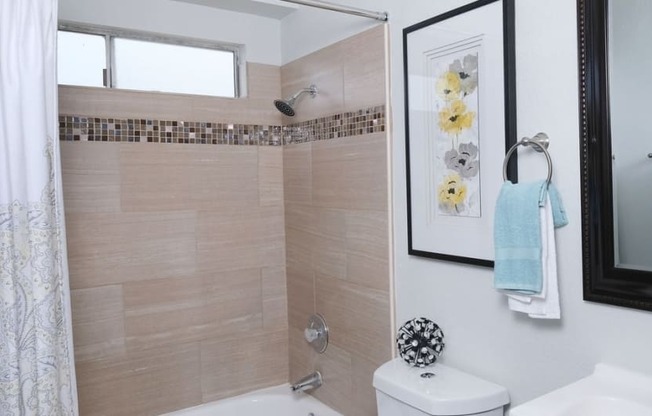 Bathroom in one bedroom Fifteen 50 apartments Las Vegas with modern natural tile in bathtub shower and a dark framed mirror above a single sink.