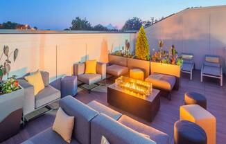 A modern outdoor seating area with a lit fire pit in the center.