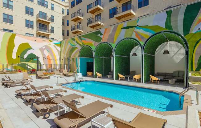 A pool surrounded by sun loungers and a building with a mural on the side.