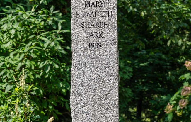 A tall, grey, rectangular memorial stone in the middle of a park.
