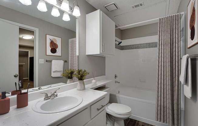 A bathroom with a white sink, toilet, and a shower with a grey shower curtain.
