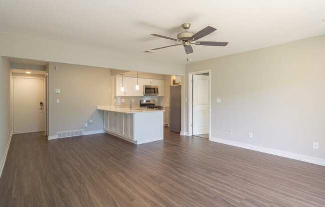 an empty living room with a kitchen in the background