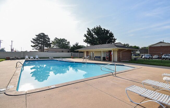 a swimming pool with chairs around it in front of a clubhouse