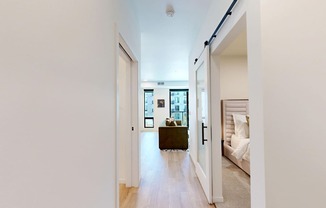 A hallway with a door on the left and a bedroom on the right.