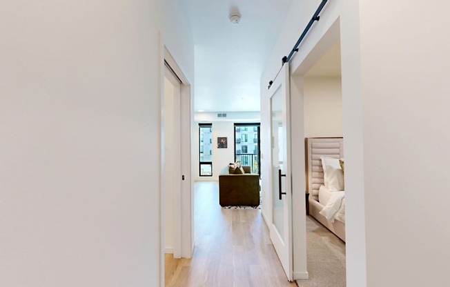 A hallway with a door on the left and a bedroom on the right.