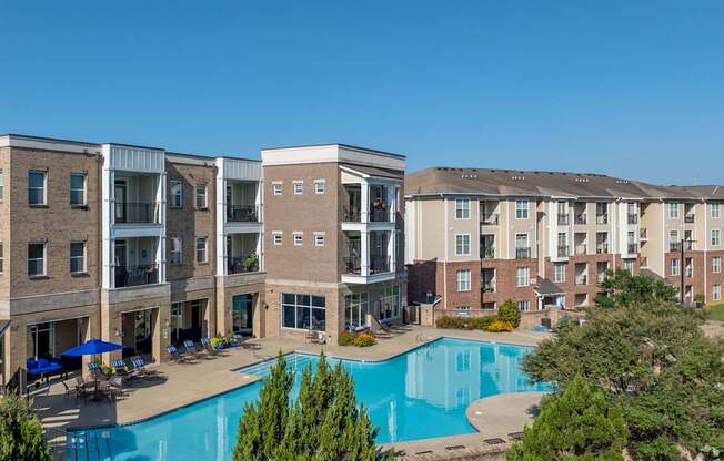 A large swimming pool is surrounded by a patio with chairs and umbrellas.