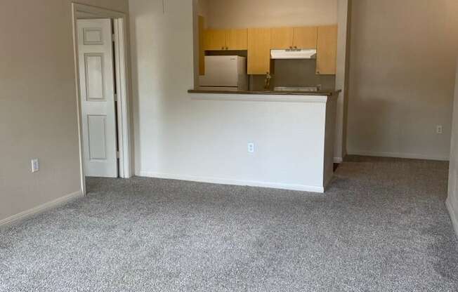 an empty living room with a ceiling fan and a kitchen