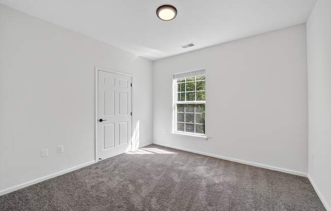 Renovated bedroom with a carpeted floor, a window, and a door.