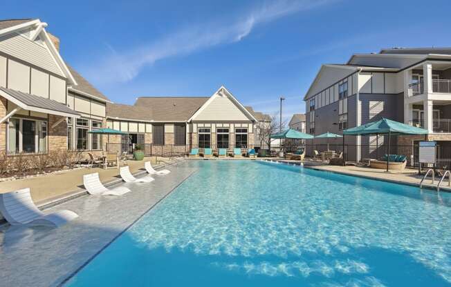 a swimming pool with chairs and umbrellas in front of a building with apartments