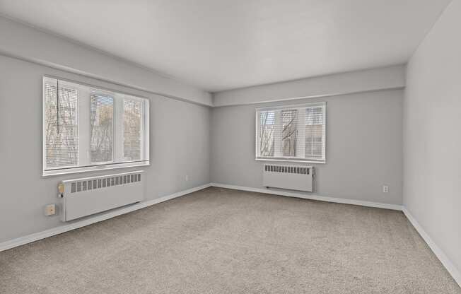 A room with a carpeted floor and two windows.