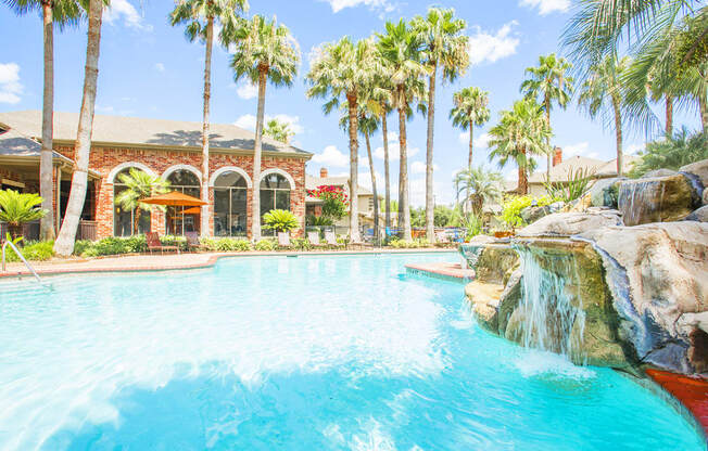 a large swimming pool with a waterfall and palm trees