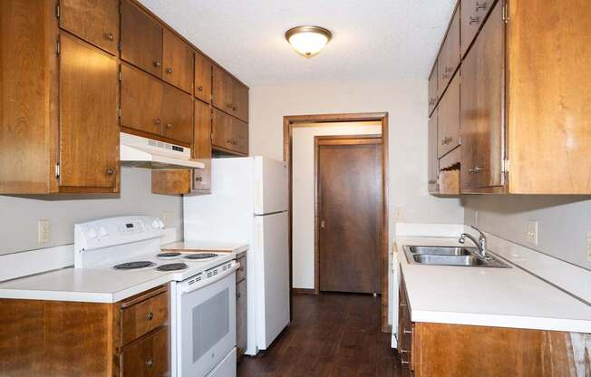 an empty kitchen with white appliances and wooden cabinets. Fargo, ND Country Club Apartments