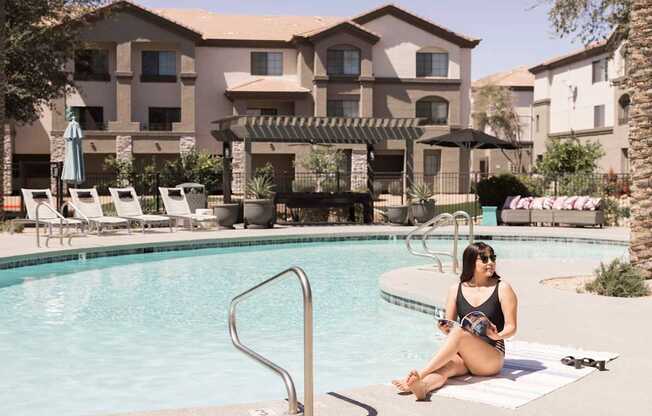 A woman is sitting by a pool in a black swimsuit.
