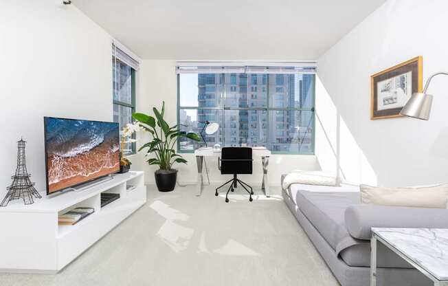A modern living room with a television, a couch, a desk, and a plant.