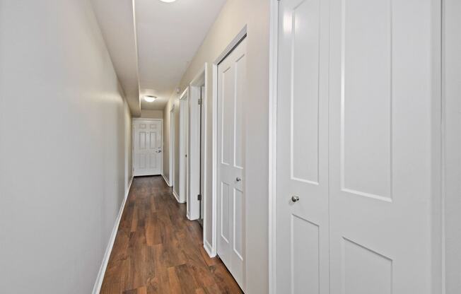 a hallway with white closets and wood floors