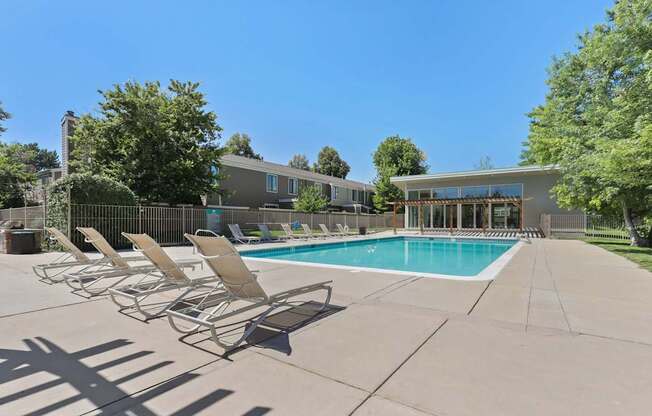 A pool with chairs around it and a building in the background.