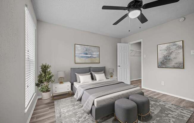 A bedroom with a large bed, a ceiling fan, and a painting on the wall.