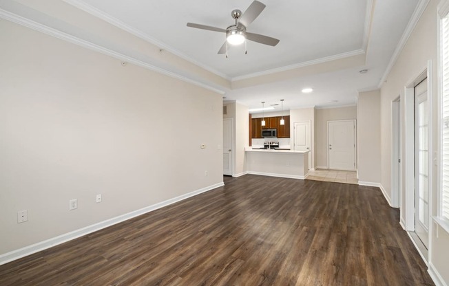 an empty living room with a ceiling fan and a kitchen