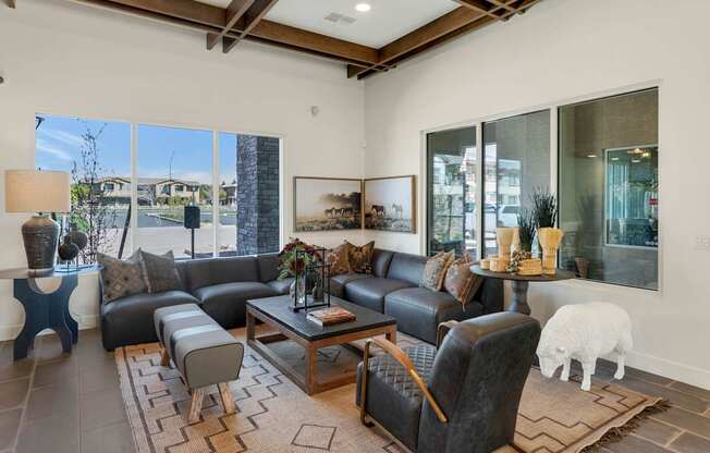 A living room with a black leather couch and a white sheep toy on the carpet.