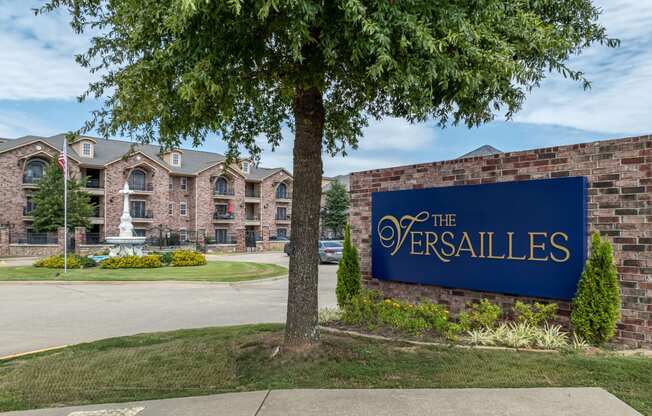 a sign for the versailles on the side of a brick building with a tree