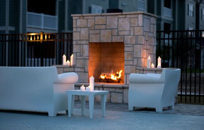 a fireplace on a patio with two white chairs and a coffee table