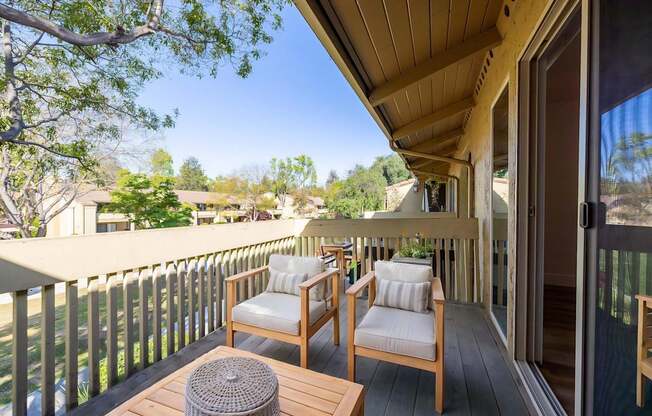 A wooden balcony with two chairs and a table.
