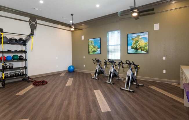 a fitness room with exercise bikes and weights on a wooden floor