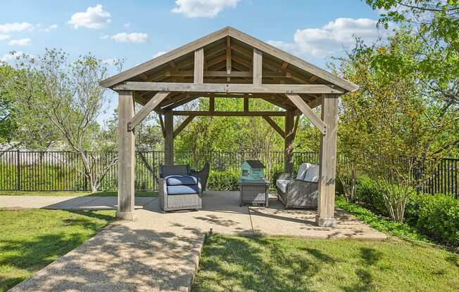 A wooden gazebo with a bench and a table in the middle of a grassy area.